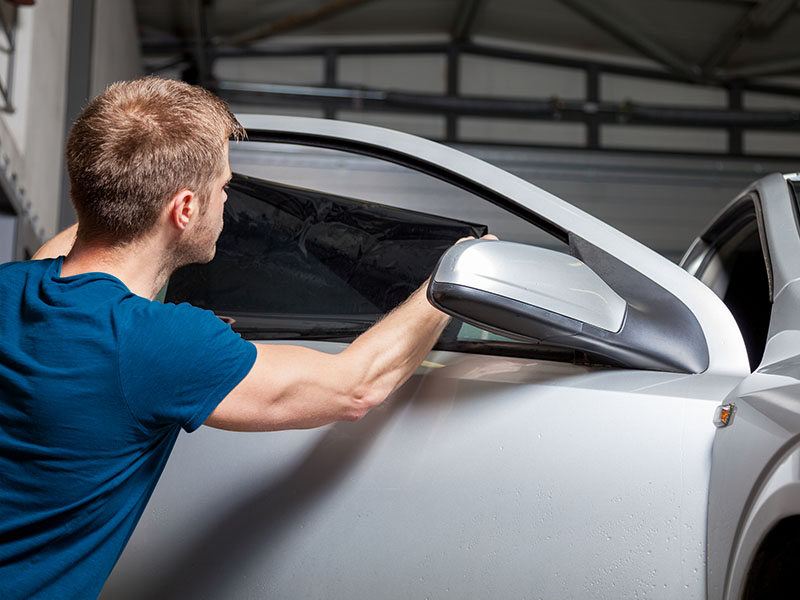 Applying tinting foil on a car window in a garage